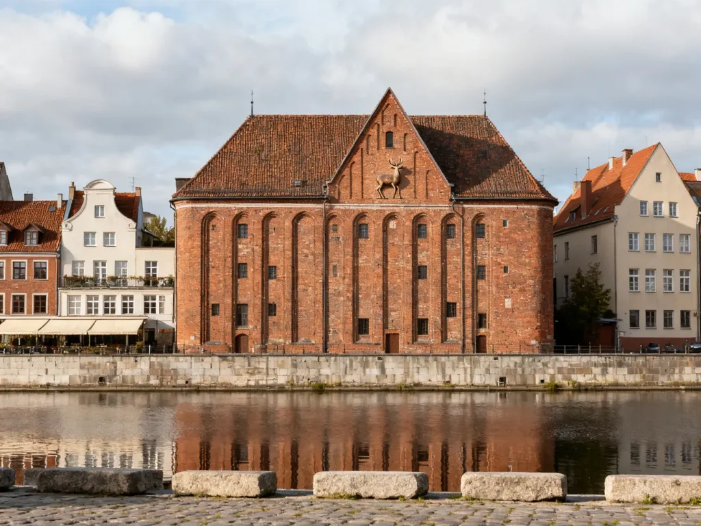 Spichlerz pod Jeleniem nad Motławą w Gdańsku, odbijający się w spokojnej wodzie, otoczony historycznymi kamienicami