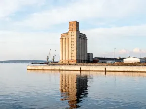 Gmach Biura Budowy Portu oświetlony złotą godziną, z frontowym wejściem, brukowanym placem i widokiem na port w tle