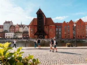 Wnętrze Miejskiej Hali Targowej z wysokimi sklepieniami, ludźmi oglądającymi stoiska z owocami, warzywami i kwiatami